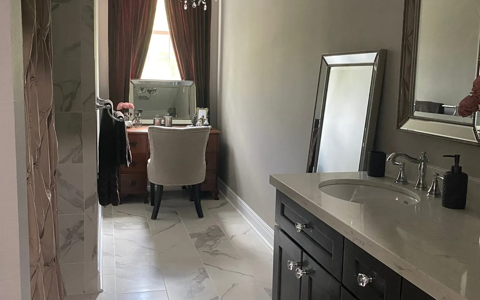The finished bathroom seen from the hallway: taupe walls, marble-look tile, a double vanity in metallic smoke, and beaded mirrors