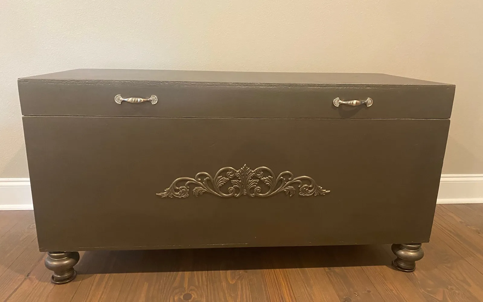 The finished toybox bench in metallic smoke with turned legs, a center applique, and silver fan pulls